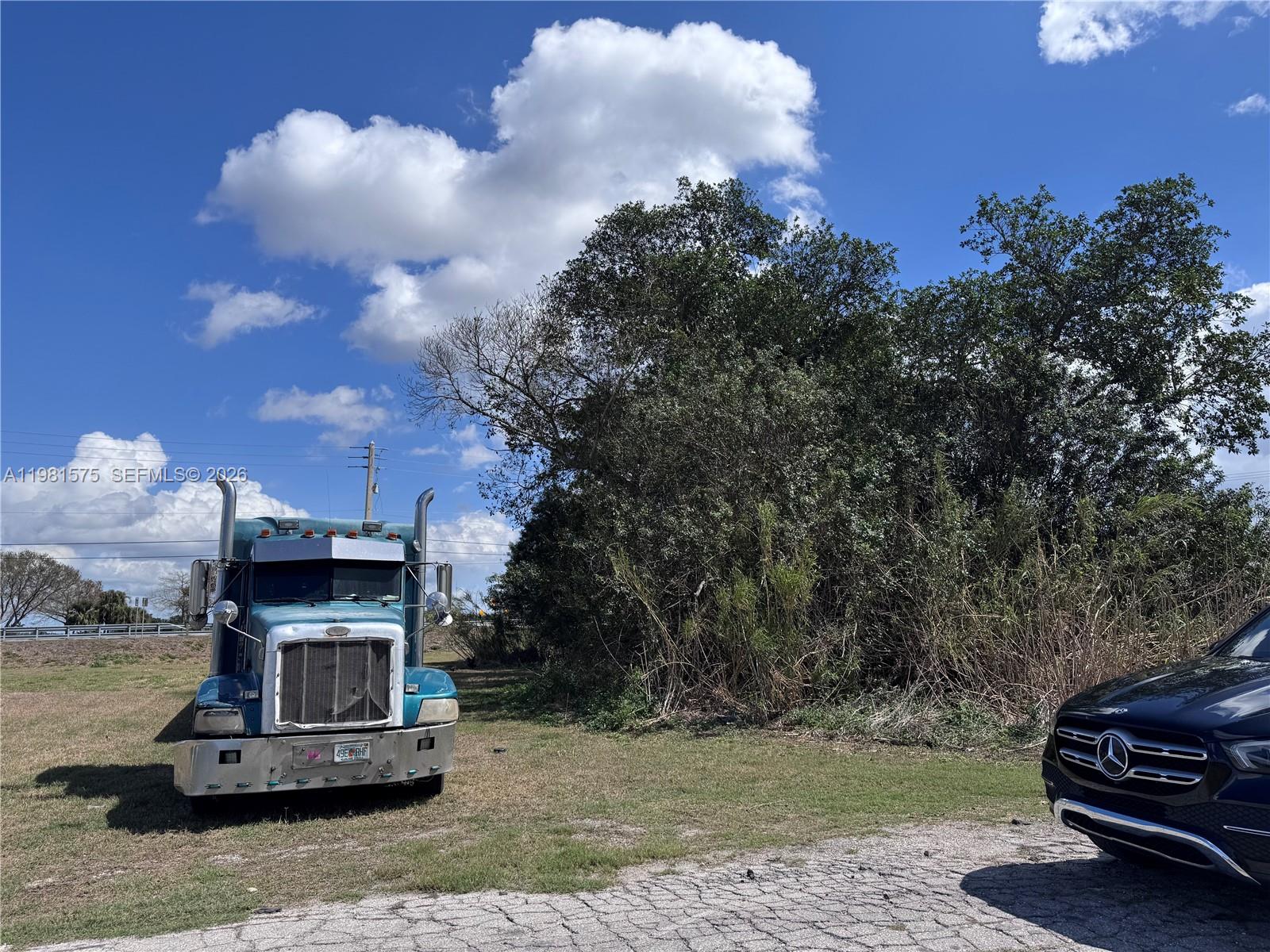 A blue semi-truck is parked on a grassy lot next to a dark SUV — 636 S Lake Ave., Pahokee FL 33476, PAHOKEE, FL