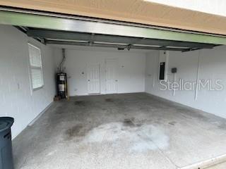 An empty two-car garage with white walls, a concrete floor, and a water heater — 10274 SW 99TH LANE, OCALA, FL