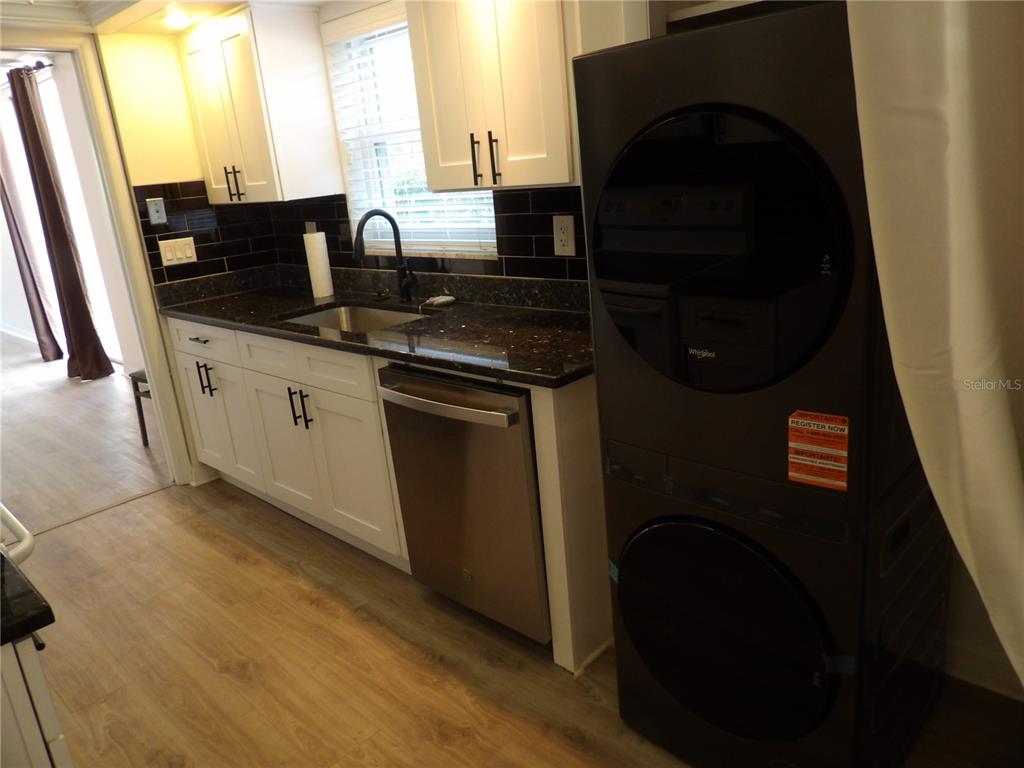 A kitchen features white cabinets, black tile backsplash, dark countertops, and a stacked laundry unit — 2623 SEVILLE BOULEVARD UNIT 111, CLEARWATER, FL