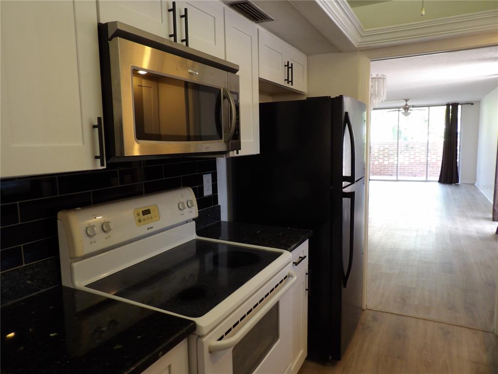 A kitchen features white cabinets, a stainless steel microwave, a white stove, and black appliances — 2623 SEVILLE BOULEVARD UNIT 111, CLEARWATER, FL