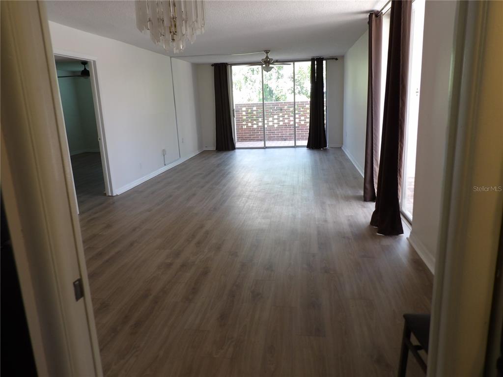A spacious living room features light wood-look flooring, a ceiling fan, and sliding glass balcony doors — 2623 SEVILLE BOULEVARD UNIT 111, CLEARWATER, FL