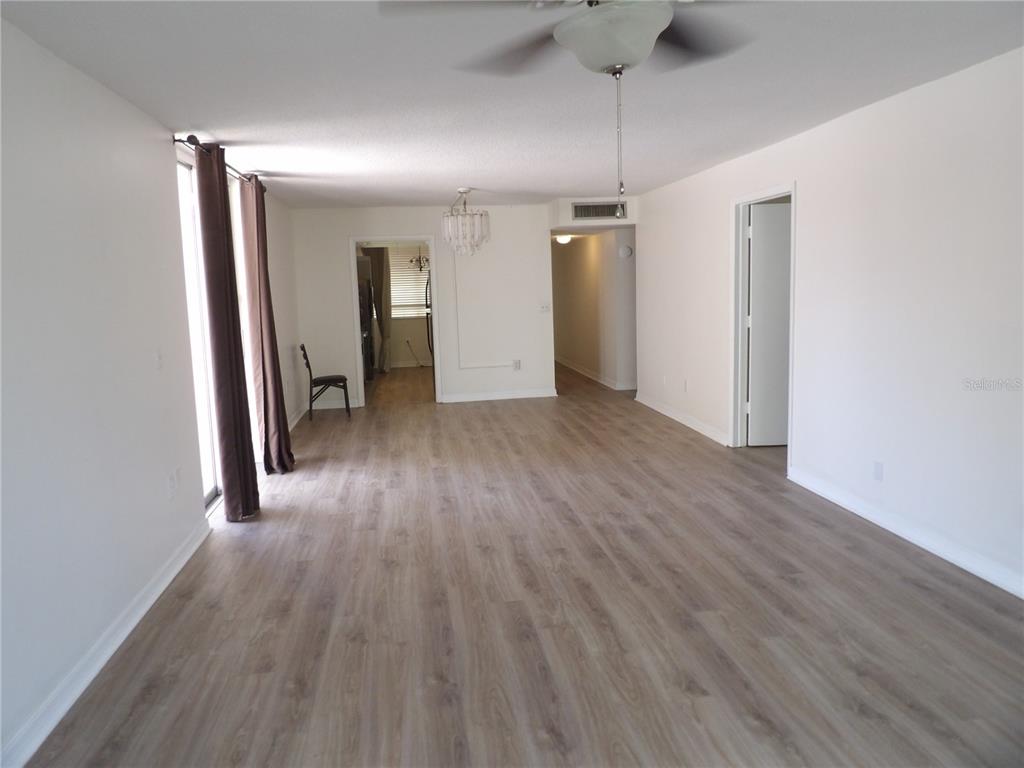 An empty living room features light wood-look flooring, white walls, and a ceiling fan — 2623 SEVILLE BOULEVARD UNIT 111, CLEARWATER, FL