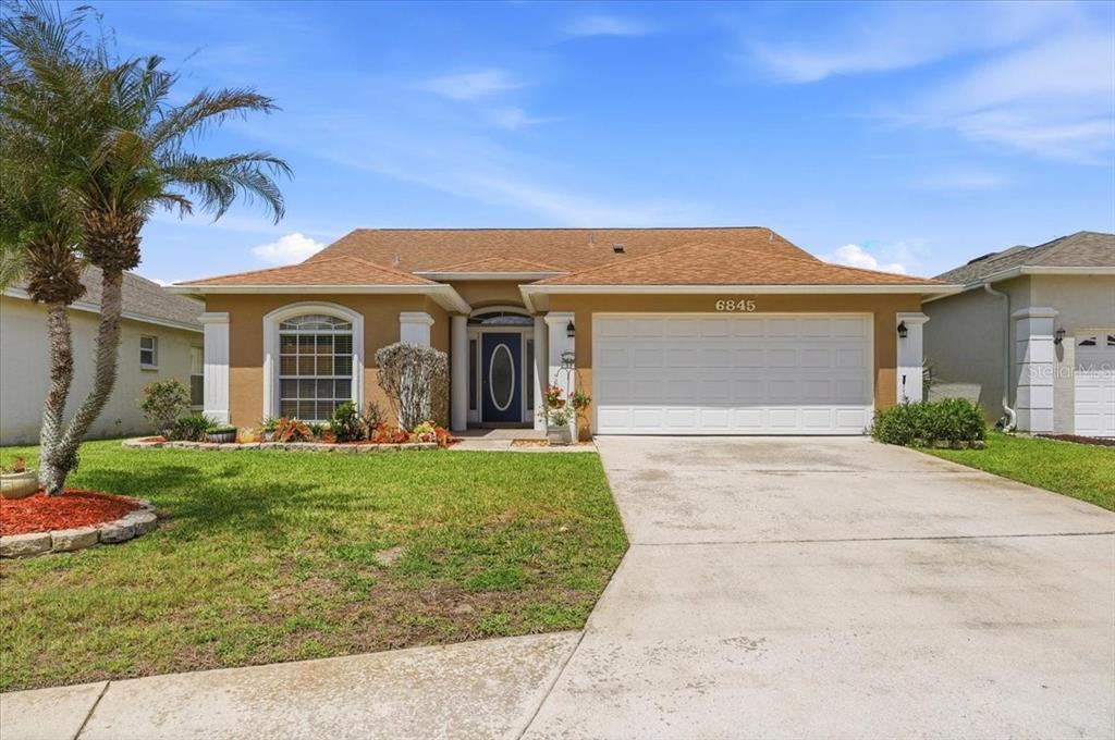 A single-story house with a tan stucco exterior, brown roof, and a two-car garage — 6845 SHIMMERING DRIVE, LAKELAND, FL