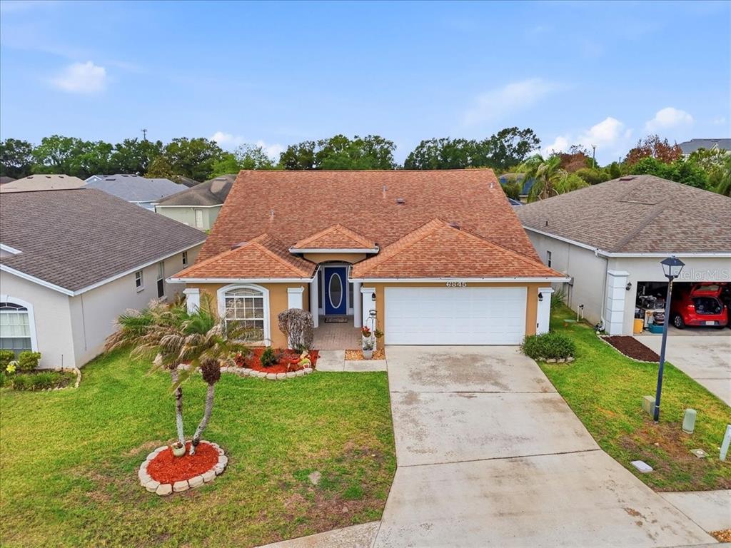 A single-story house with a tan exterior, a brown shingled roof, and a concrete driveway — 6845 SHIMMERING DRIVE, LAKELAND, FL