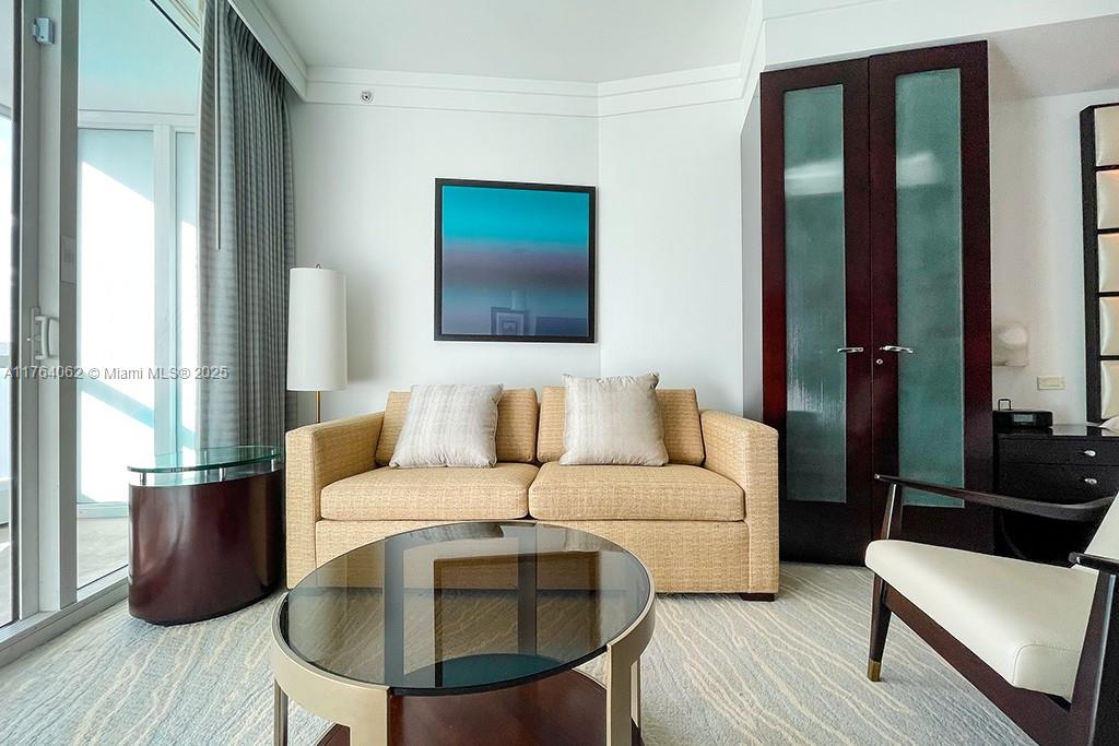 A living room features a beige sofa, a glass coffee table, and dark wood doors — 4391 Collins ave # 616, Miami Beach FL 33140, MIAMI BEACH, FL