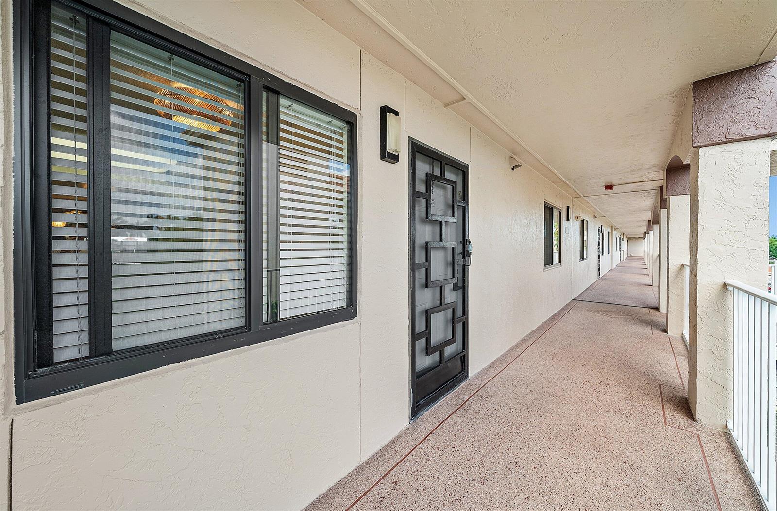 An exterior walkway leads past a window and a black metal security door of a unit — 6065 Pointe Regal Circle, Delray Beach FL 33484, DELRAY BEACH, FL