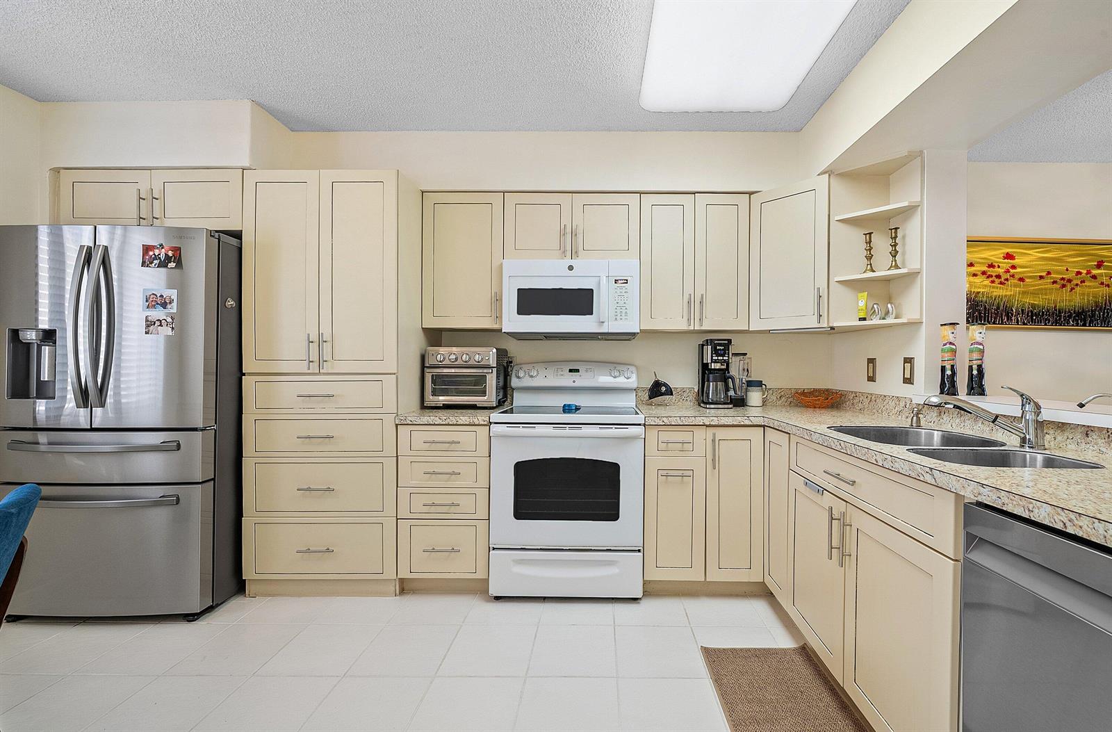 A kitchen with cream-colored cabinets, stainless steel appliances, and light-colored granite countertops — 6065 Pointe Regal Circle, Delray Beach FL 33484, DELRAY BEACH, FL