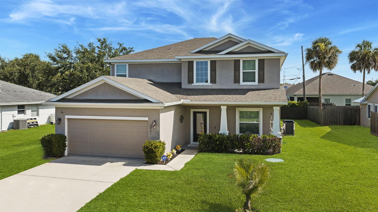 A two-story suburban house with a tan stucco exterior, a two-car garage, and green lawns — 2241 SW Abalon Circle, FL 34953, FL