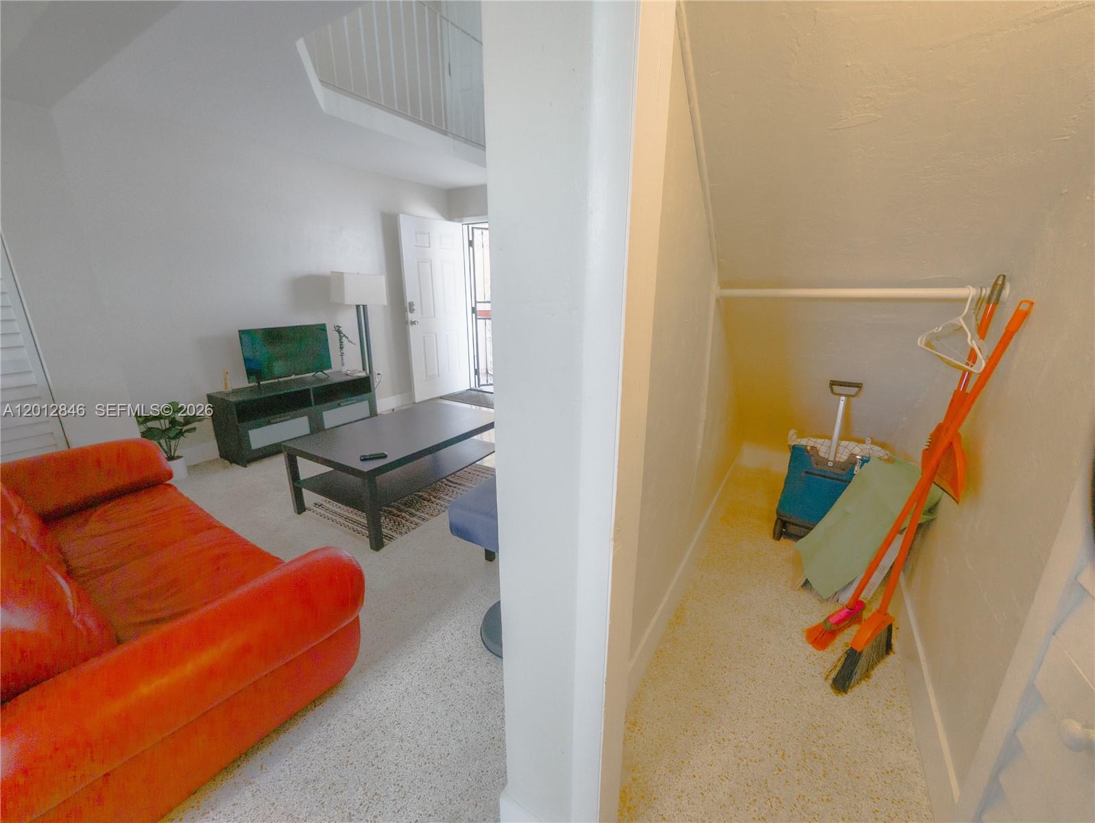 A living room with a red sofa and a small under-stair storage closet with cleaning supplies — 1220 SW 5th St # 16, Miami FL 33135, MIAMI, FL