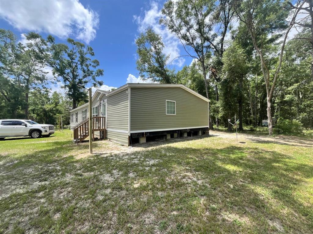 The exterior of a light green manufactured home with a wooden deck and exposed foundation — 21619 41ST DRIVE, LAKE CITY, FL