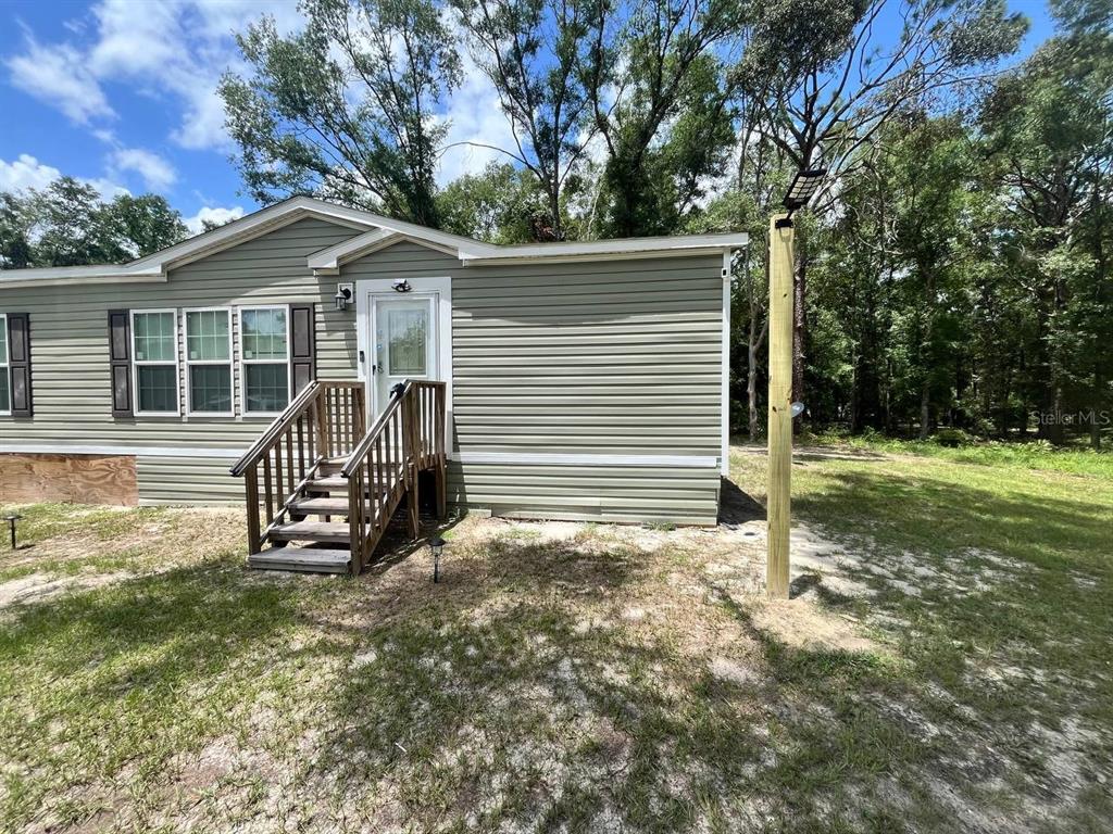 A light green mobile home exterior features a wooden staircase leading to a white door — 21619 41ST DRIVE, LAKE CITY, FL