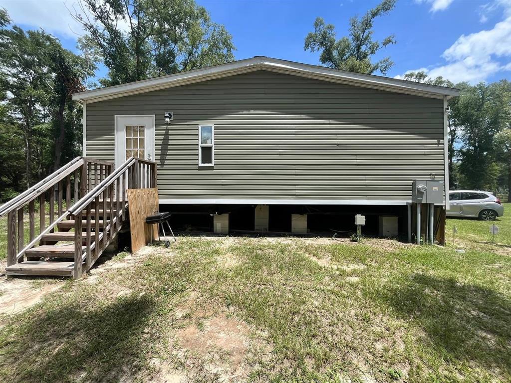 An exterior view of a manufactured home with vinyl siding, wooden stairs, and exposed piers — 21619 41ST DRIVE, LAKE CITY, FL
