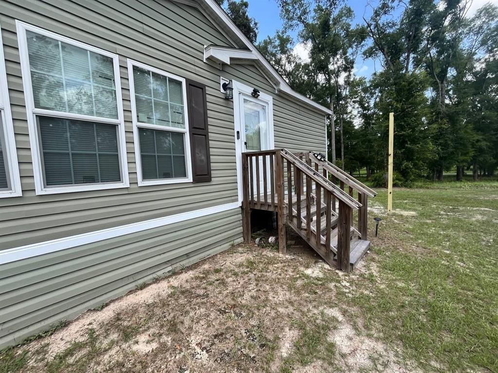 Exterior view of a light green vinyl-sided house with a wooden staircase and door — 21619 41ST DRIVE, LAKE CITY, FL