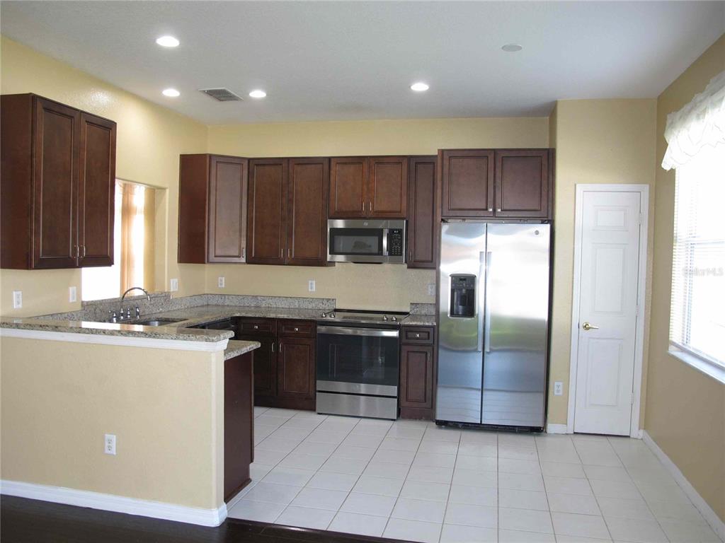 A kitchen features dark wood cabinets, granite countertops, stainless steel appliances, and white tile flooring — 925 TORREY PINE DRIVE, WINTER SPRINGS, FL