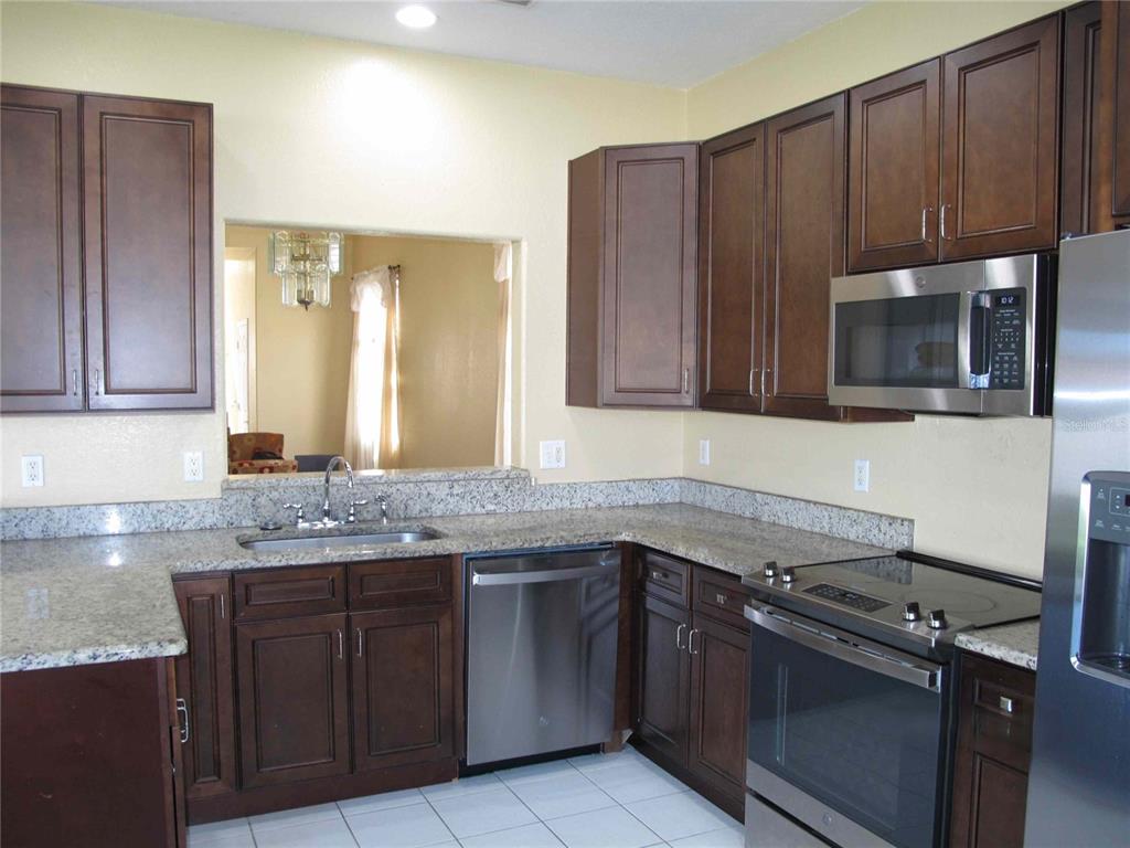 A kitchen features dark wood cabinets, granite countertops, stainless steel appliances, and a pass-through window — 925 TORREY PINE DRIVE, WINTER SPRINGS, FL