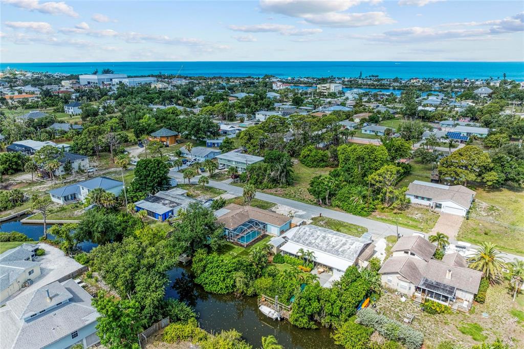 An aerial view shows houses nestled among lush trees near a canal and the ocean — 312 WINFIELD WAY, NOKOMIS, FL