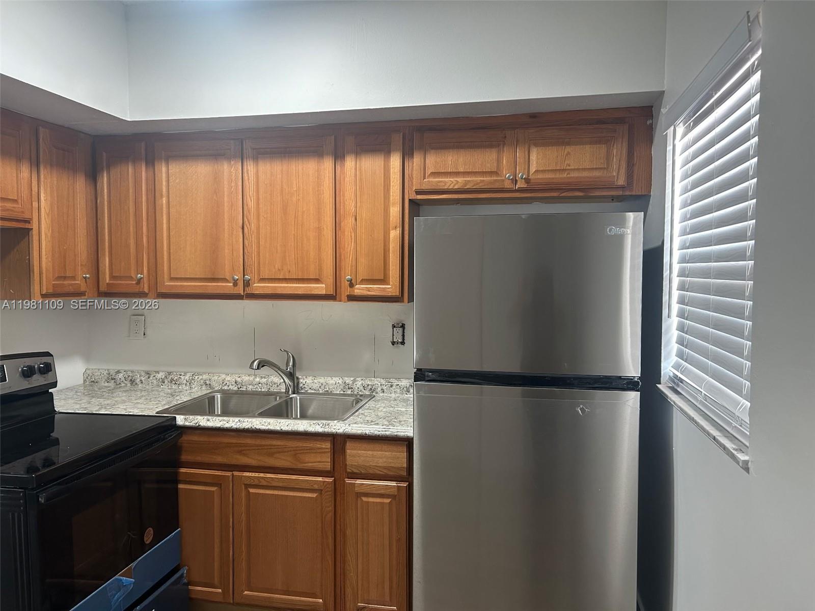 A kitchen features wood cabinets, a stainless steel refrigerator, and a double-basin sink — 730 SW 4th St # A, Dania Beach FL 33004, DANIA BEACH, FL
