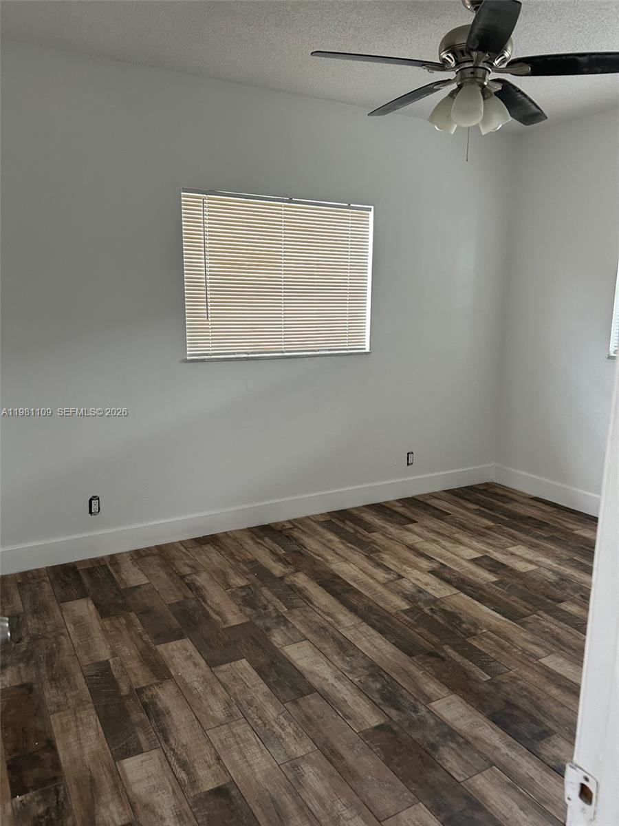 An empty bedroom features white walls, wood-look tile flooring, a ceiling fan, and a window — 730 SW 4th St # A, Dania Beach FL 33004, DANIA BEACH, FL