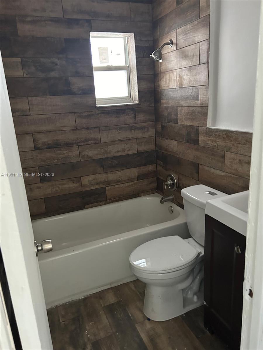 A small bathroom features wood-look tile walls, a white bathtub, a toilet, and a vanity — 730 SW 4th St # A, Dania Beach FL 33004, DANIA BEACH, FL