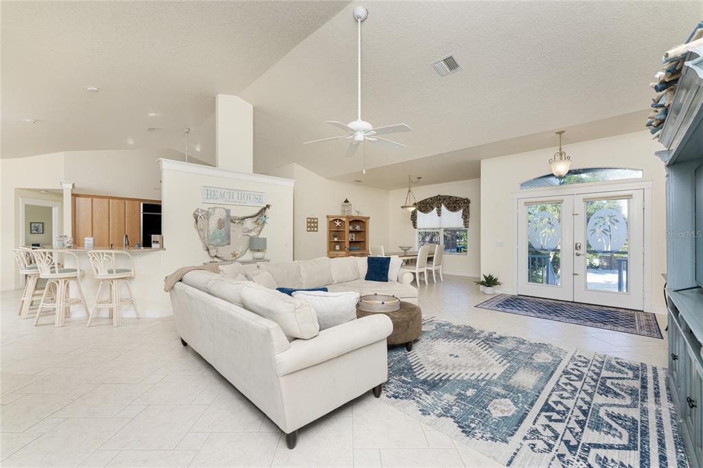 A bright, open-concept living room features a white sectional sofa, tile flooring, and kitchen access — 4151 N BEACH ROAD, ENGLEWOOD, FL