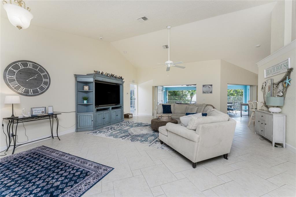 A living room features vaulted ceilings, tile flooring, a large wall clock, and a blue entertainment center — 4151 N BEACH ROAD, ENGLEWOOD, FL