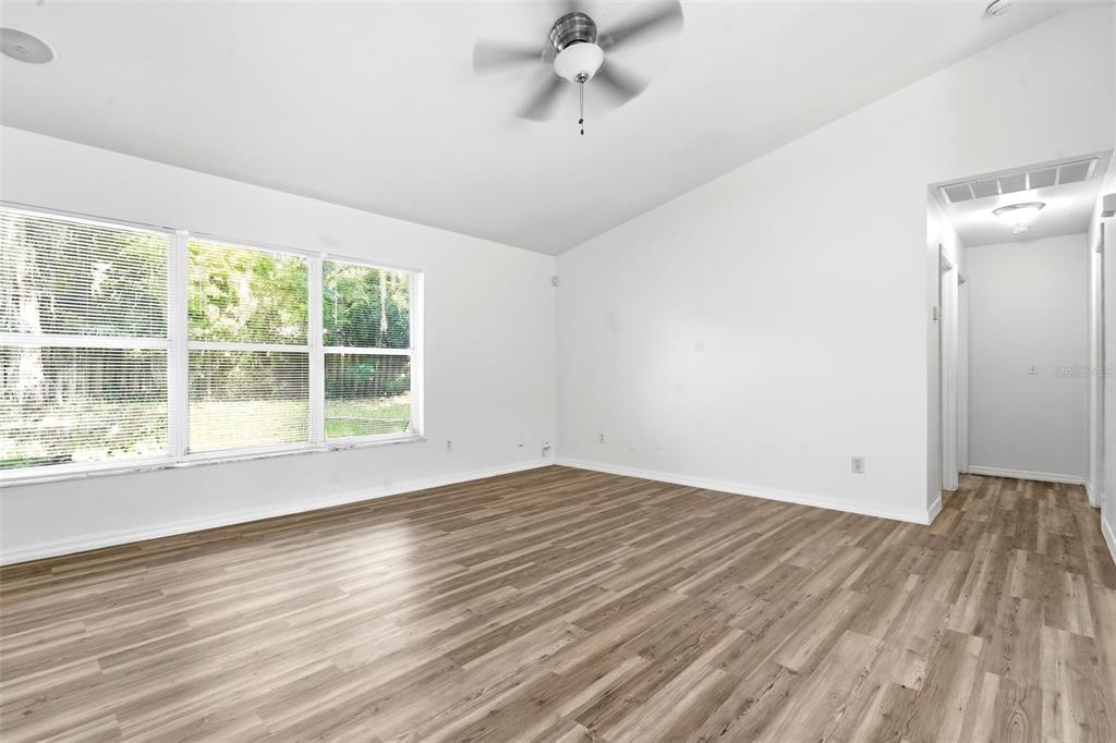 An empty room features light wood-look flooring, white walls, a ceiling fan, and large windows — 3128 MANGO TREE DRIVE, EDGEWATER, FL