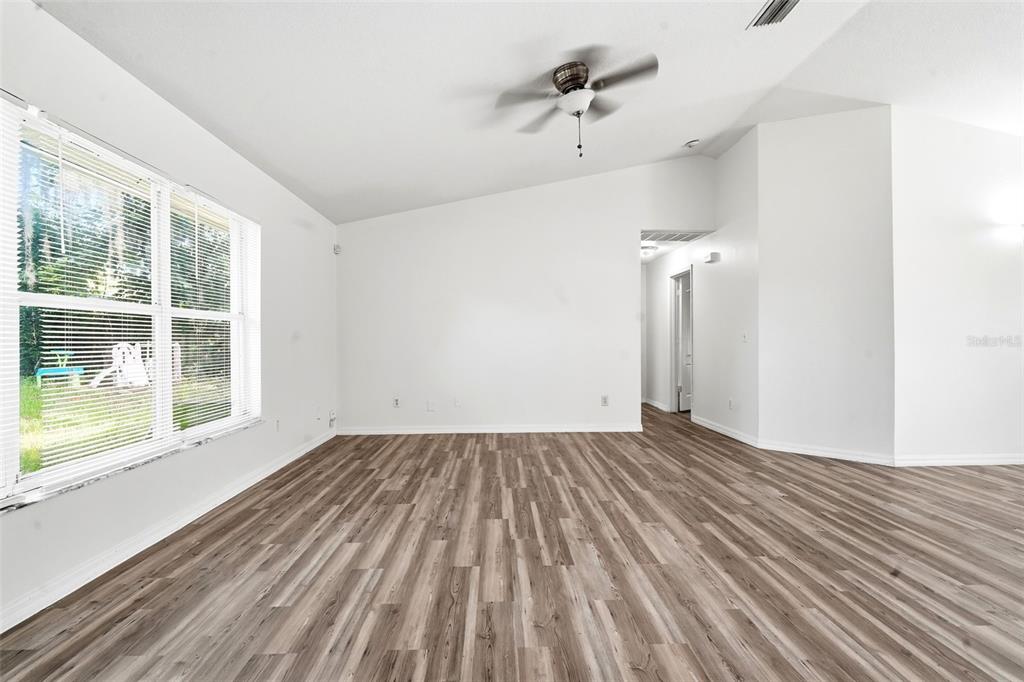 An empty room features wood-look flooring, white walls, a ceiling fan, and large windows — 3128 MANGO TREE DRIVE, EDGEWATER, FL