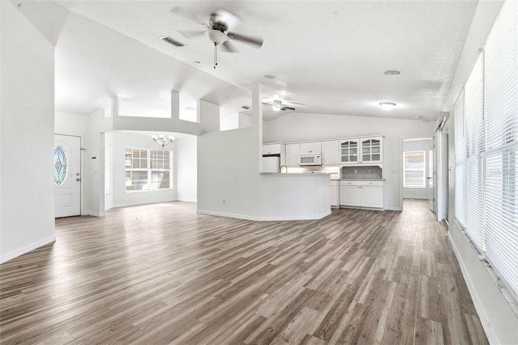 An open-concept living area with wood-look flooring, a white kitchen, and vaulted ceilings — 3128 MANGO TREE DRIVE, EDGEWATER, FL