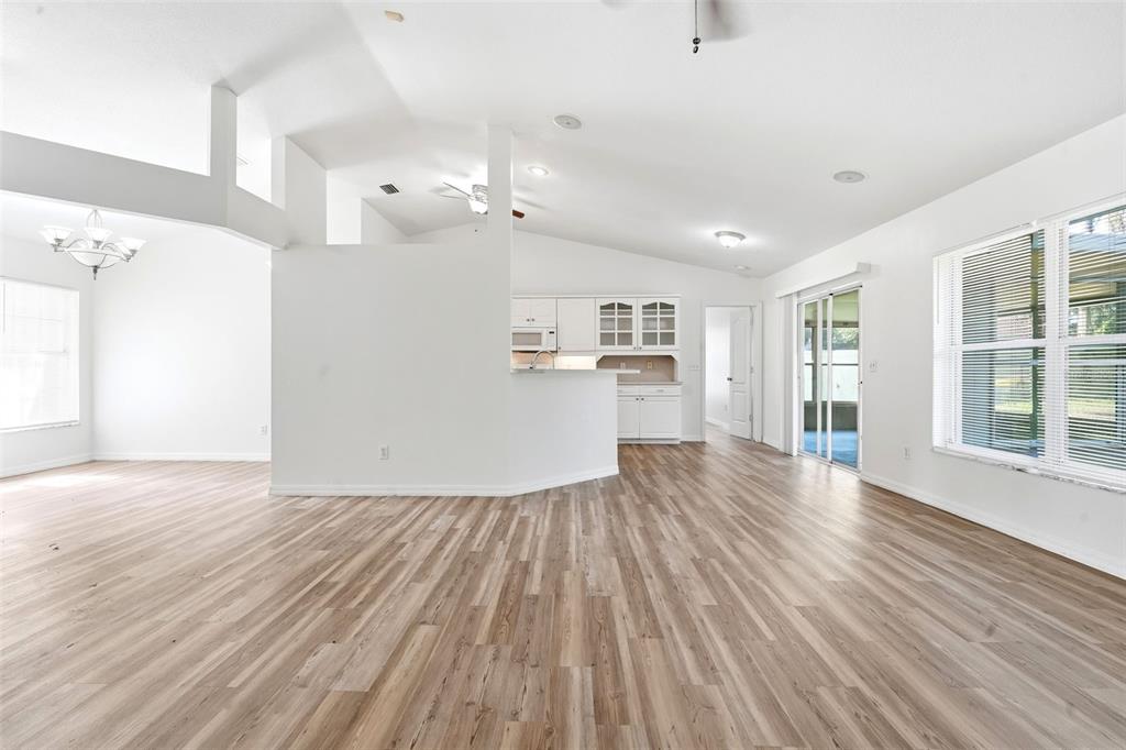 An open-concept living area features light wood-look flooring, white walls, and a central kitchen island — 3128 MANGO TREE DRIVE, EDGEWATER, FL