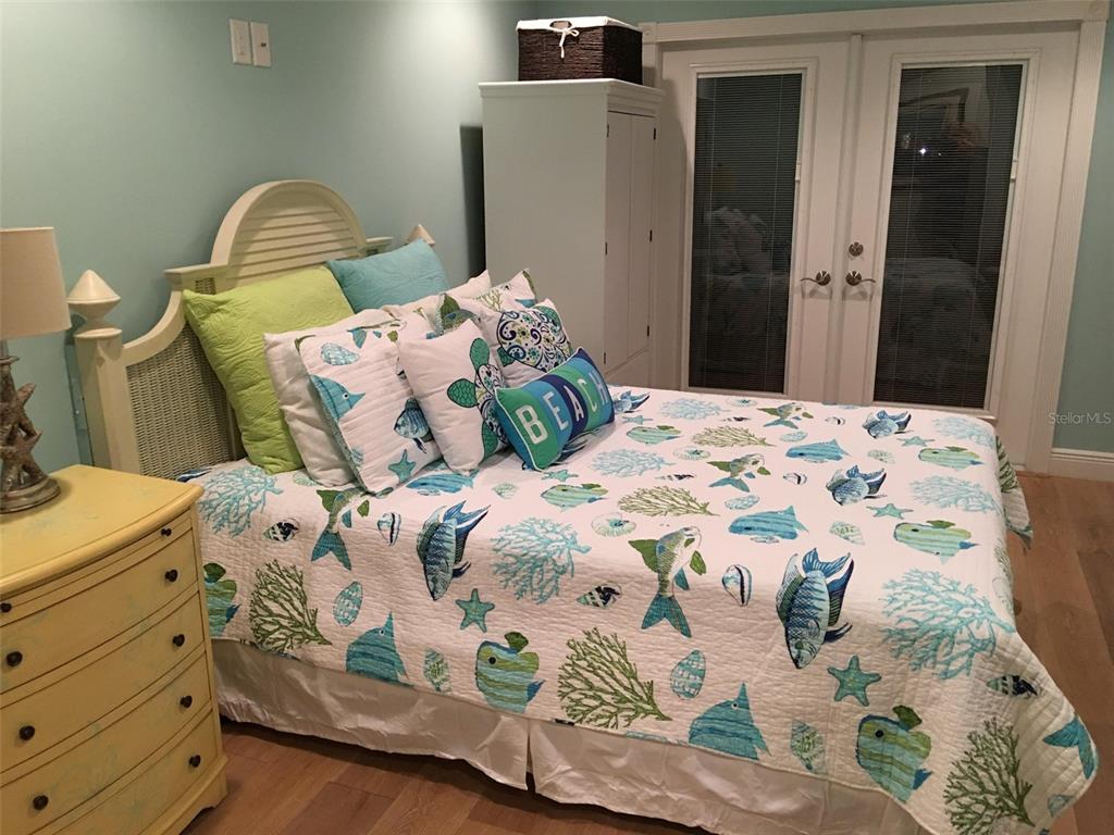 A bedroom features a bed with a beach-themed quilt, a yellow dresser, and French doors — 513 GUNWALE LANE, LONGBOAT KEY, FL