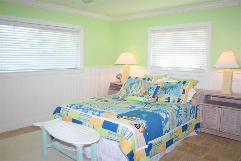 A bedroom features light green walls, white wainscoting, tile flooring, and a tropical-themed quilt — 513 GUNWALE LANE, LONGBOAT KEY, FL