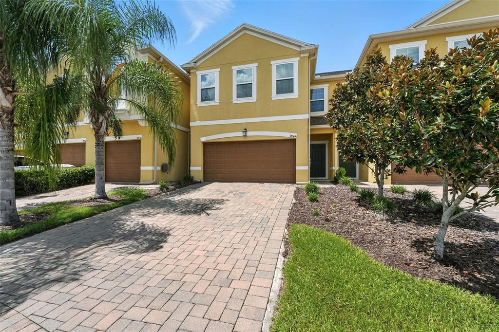 A two-story yellow townhouse with a paved driveway, a two-car garage, and a palm tree — 9944 RED EAGLE DRIVE, ORLANDO, FL