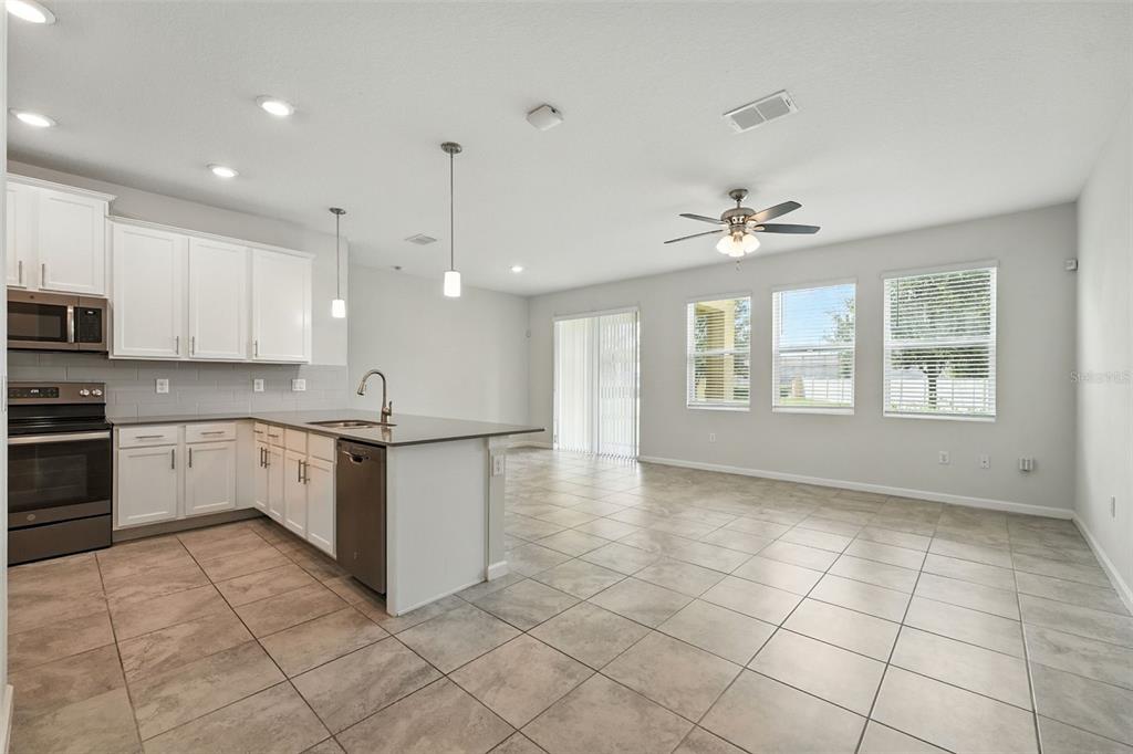 A kitchen with white cabinets and stainless steel appliances opens into a tiled living area — 9944 RED EAGLE DRIVE, ORLANDO, FL