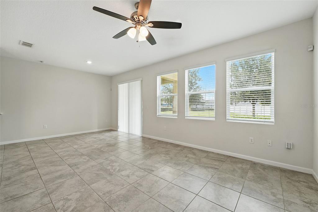 A bright, empty living room features light gray tile flooring, a ceiling fan, and windows — 9944 RED EAGLE DRIVE, ORLANDO, FL