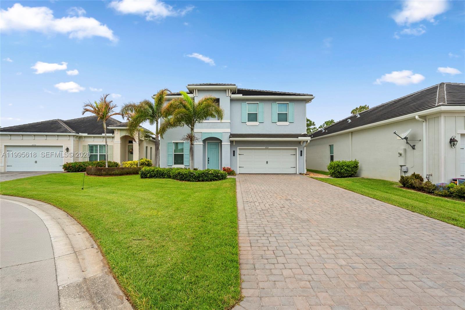 A two-story light blue house features a paved driveway, palm trees, and a green lawn — 4764 SW Briarwood Ct, Stuart FL 34997, STUART, FL