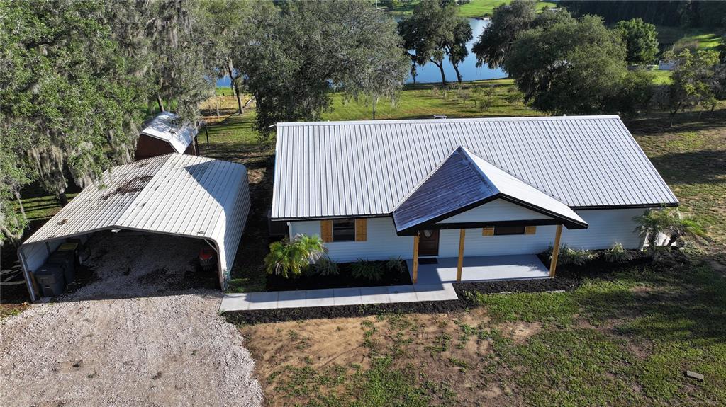 A white house with a metal roof, a covered porch, and wooden shutters sits on a lawn — 1100 GOLDEN BOUGH ROAD, LAKE WALES, FL