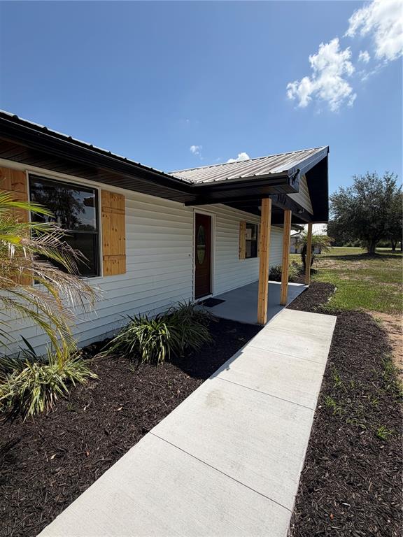 A single-story house with white siding, a metal roof, and a covered front porch — 1100 GOLDEN BOUGH ROAD, LAKE WALES, FL