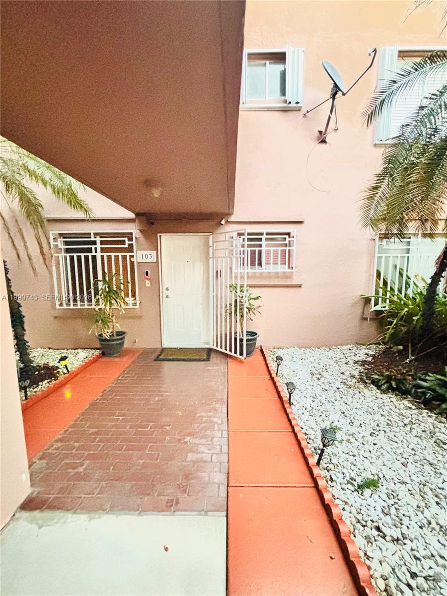The exterior of a peach-colored building features a brick walkway leading to unit 103 — 2310 W 74th St # 103, Hialeah FL 33016, HIALEAH, FL