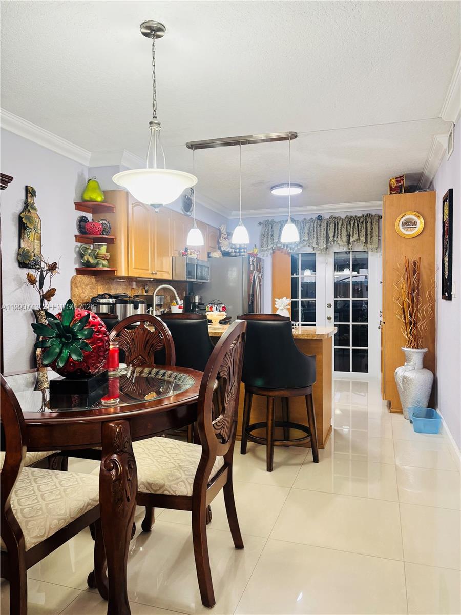 A dining area with a round wooden table sits adjacent to a kitchen with bar seating — 2310 W 74th St # 103, Hialeah FL 33016, HIALEAH, FL