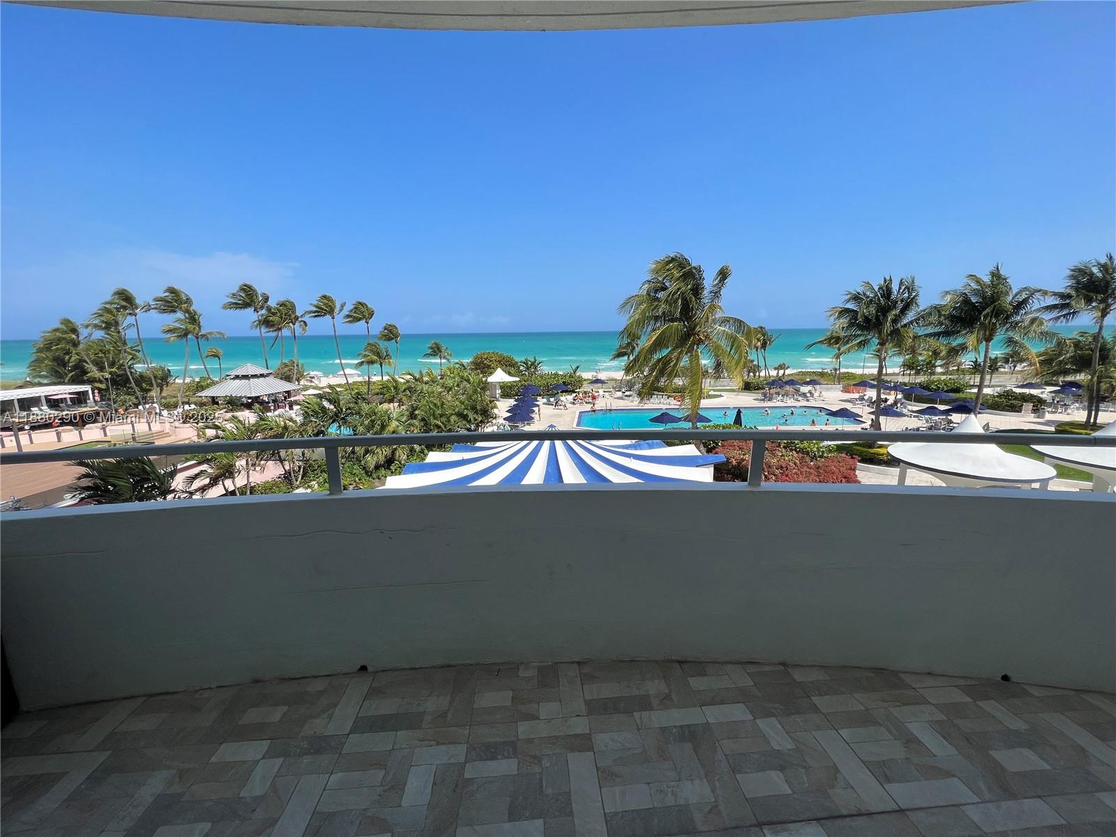 A balcony overlooks a swimming pool, palm trees, and the ocean under a clear sky — 5161 Collins Ave # 514, Miami Beach FL 33140, MIAMI BEACH, FL