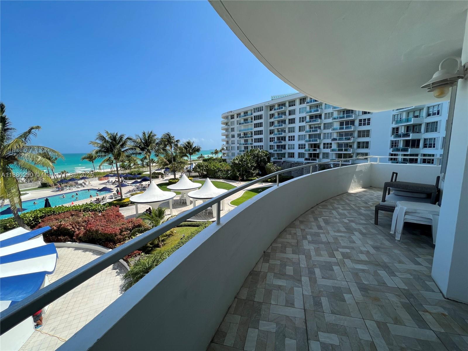 A balcony with tiled flooring overlooks a swimming pool, palm trees, and the ocean — 5161 Collins Ave # 514, Miami Beach FL 33140, MIAMI BEACH, FL