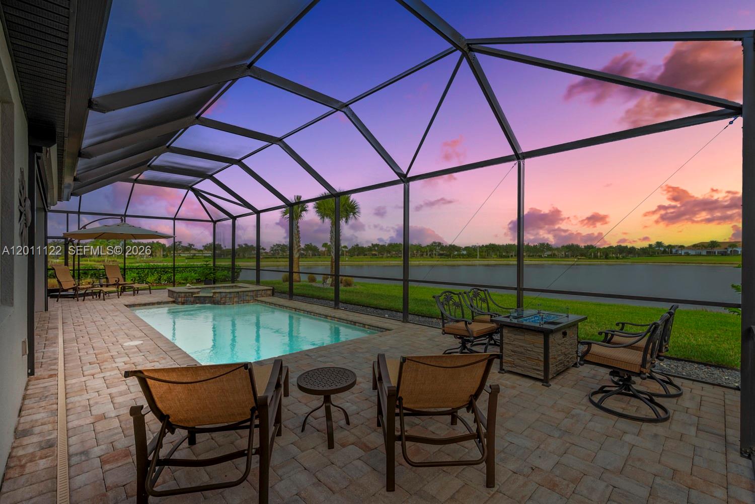 A screened-in patio features a pool, spa, and outdoor seating overlooking a lake at sunset — 6279 LIBERTY ST, Ave Maria FL 34142, AVE MARIA, FL