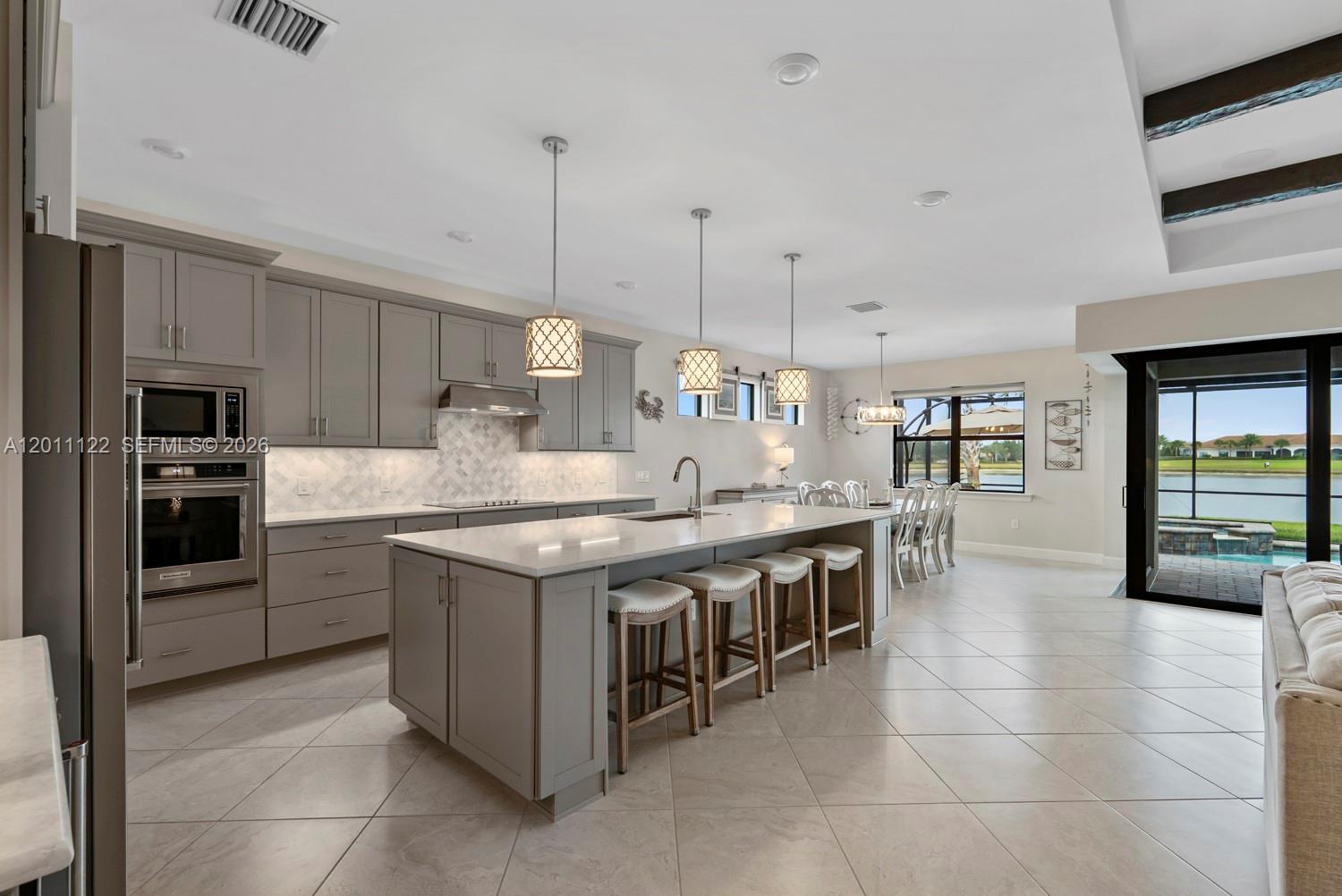 A modern kitchen features grey cabinetry, a large island with bar seating, and tile flooring — 6279 LIBERTY ST, Ave Maria FL 34142, AVE MARIA, FL