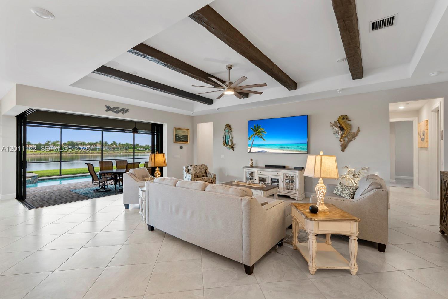 A living room with exposed ceiling beams, a large television, and a view of a pool — 6279 LIBERTY ST, Ave Maria FL 34142, AVE MARIA, FL