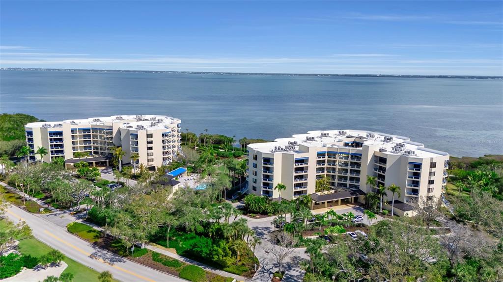 An aerial view shows two large, multi-story apartment buildings situated along a waterfront — 2110 HARBOURSIDE DRIVE UNIT 523, LONGBOAT KEY, FL