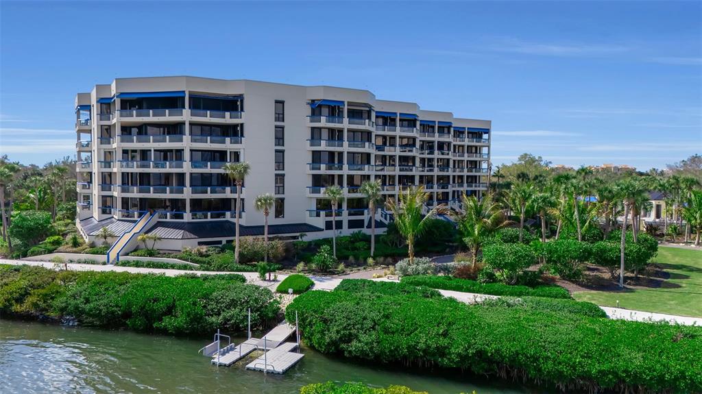 An exterior view of a multi-story apartment building situated near a canal and greenery — 2110 HARBOURSIDE DRIVE UNIT 523, LONGBOAT KEY, FL