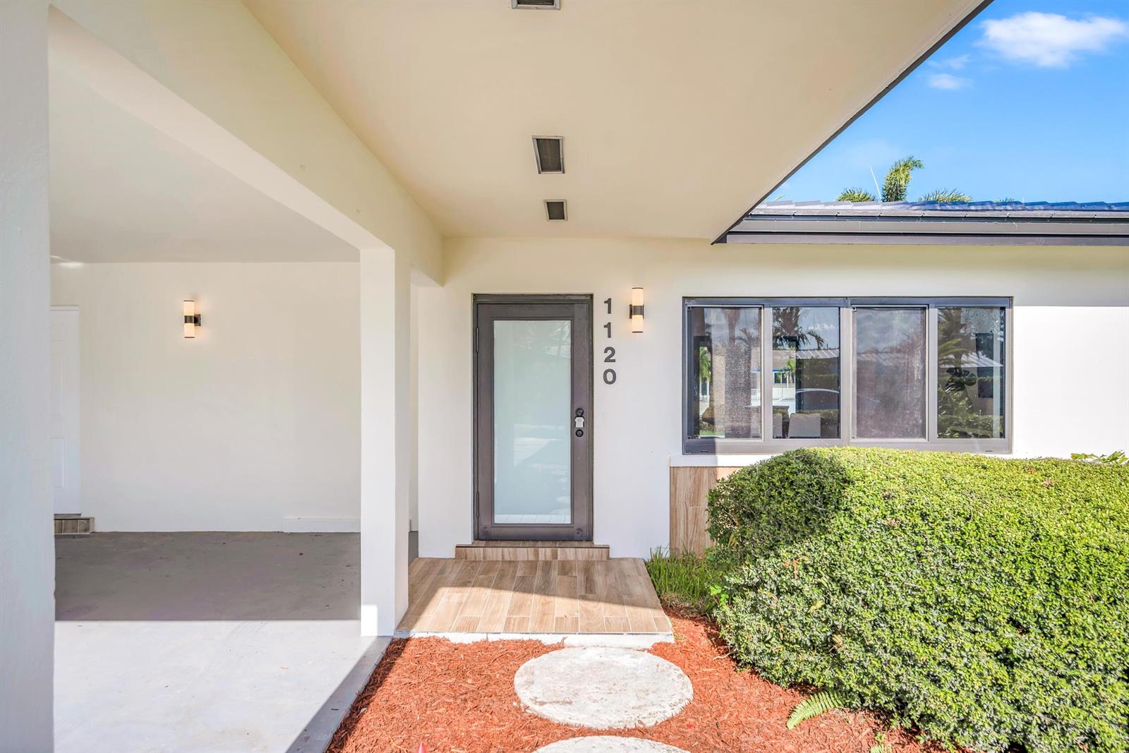 The exterior of a home features a glass-paneled front door, wood-look tile, and a bush — 1120 SE 9th Avenue, Pompano Beach FL 33060, POMPANO BEACH, FL