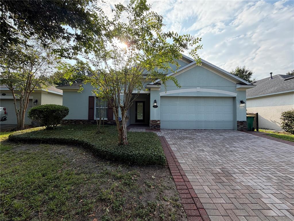 A single-story house with a light blue exterior, a paver driveway, and a front garden — 115 GLADESDOWN COURT, DELAND, FL