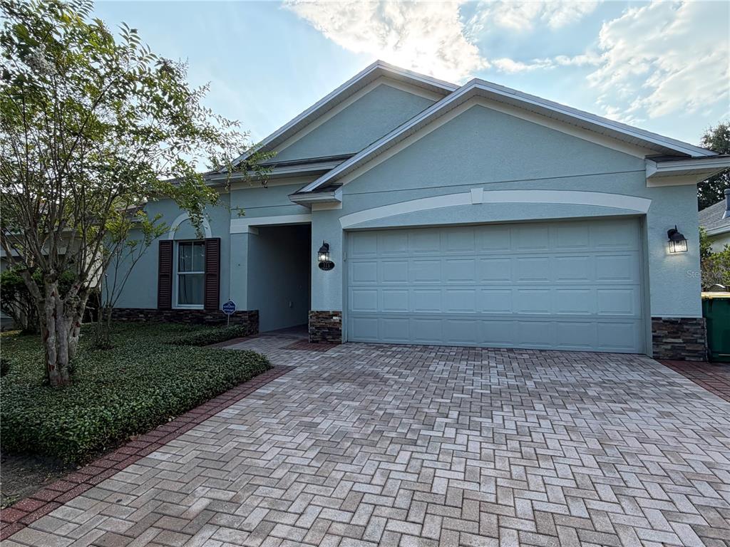 A light blue single-story house features a two-car garage and a paved brick driveway — 115 GLADESDOWN COURT, DELAND, FL