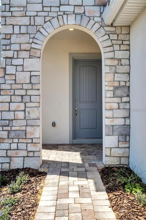 A stone-faced arched entryway leads to a gray front door with a paver walkway — 15730 VETTA DRIVE, MONTVERDE, FL